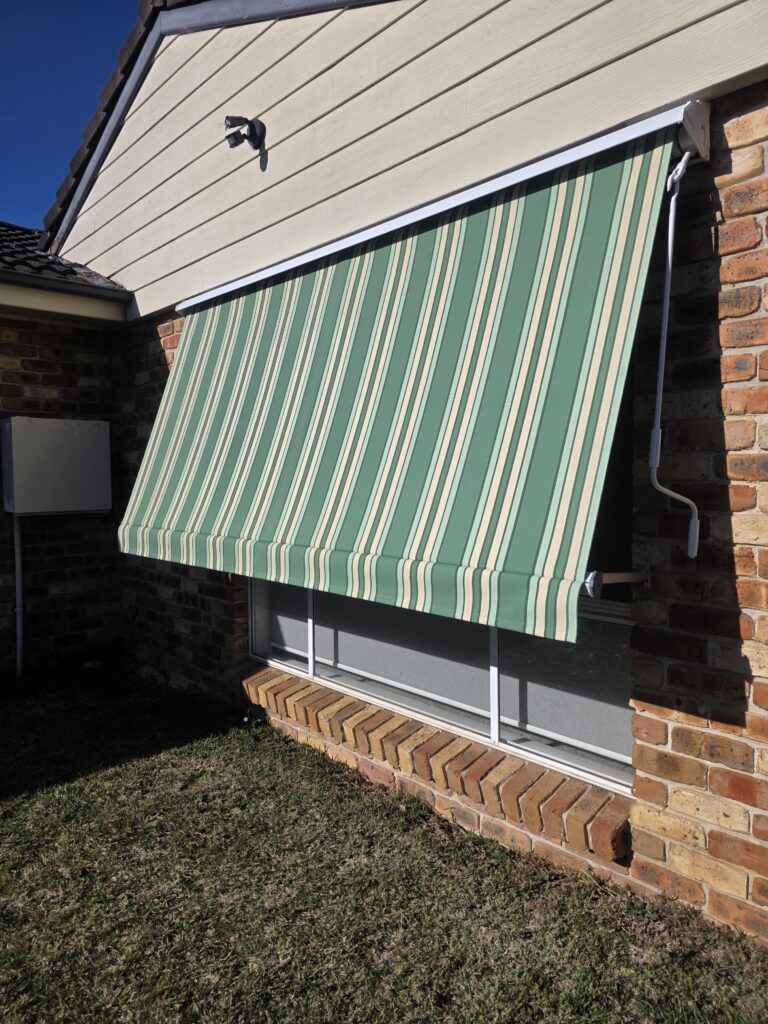 Systems 2000 pivot arm awning in green striped canvas on a brick home window