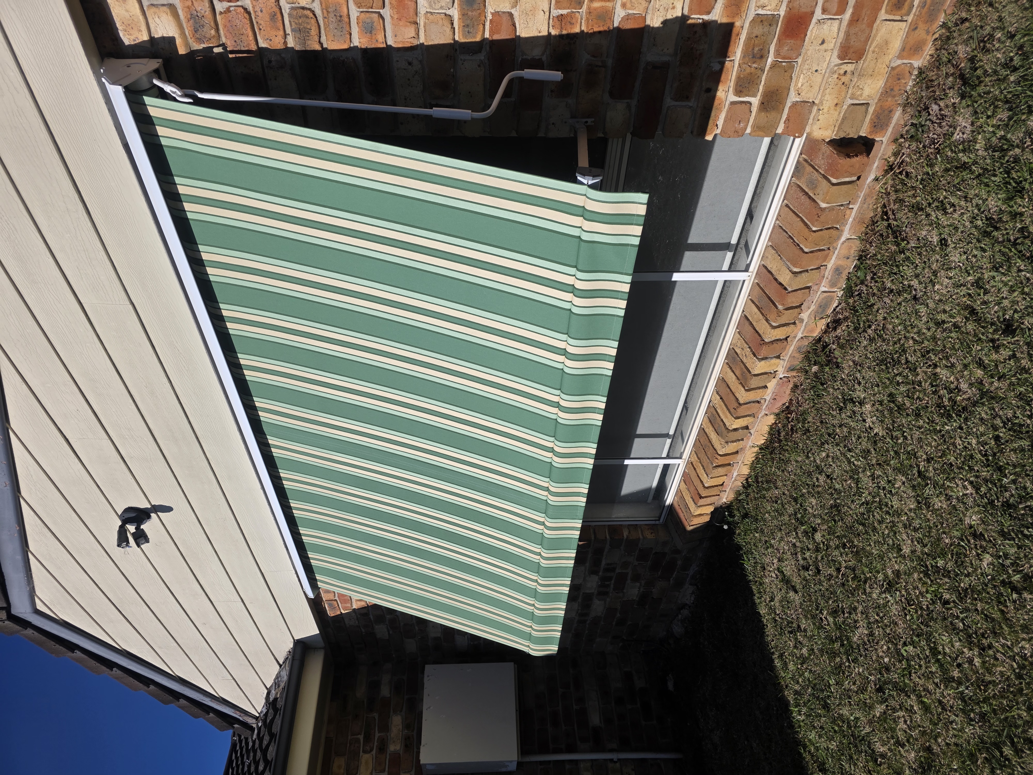 Systems 2000 pivot arm awning in green striped canvas on a brick home window