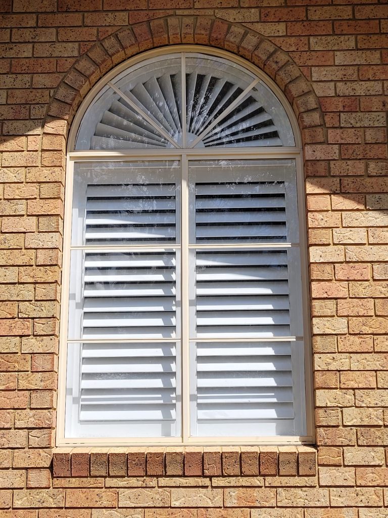 old arched window pictured from outside with shutterblinds visible inside