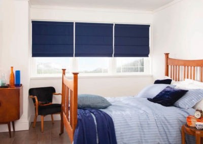 small navy blue roller blinds in a room with blue bed linen and timber furniture