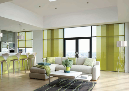 a large living area with white and wood furnishings and green accents in cushions and panel curtains